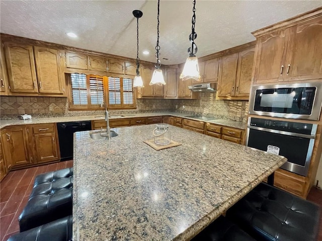 kitchen with a breakfast bar area, under cabinet range hood, black appliances, an island with sink, and decorative light fixtures