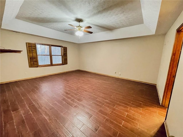 empty room with baseboards, a raised ceiling, a ceiling fan, dark wood-style flooring, and a textured ceiling