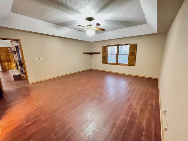 empty room with baseboards, ceiling fan, wood finished floors, a tray ceiling, and a textured ceiling