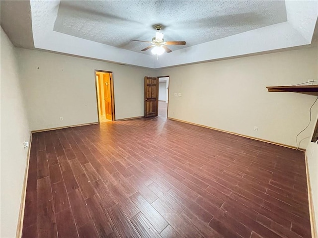 empty room with dark wood-style floors, a raised ceiling, ceiling fan, and a textured ceiling