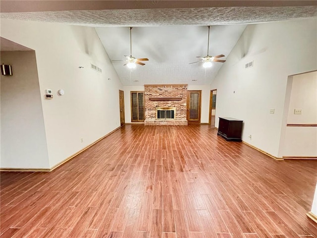 unfurnished living room with high vaulted ceiling, a fireplace, wood finished floors, and visible vents