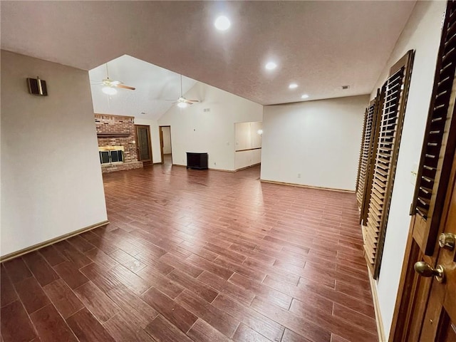 unfurnished living room featuring wood tiled floor, a fireplace, vaulted ceiling, and a ceiling fan