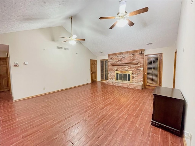 unfurnished living room featuring visible vents, a brick fireplace, vaulted ceiling, a textured ceiling, and light wood-type flooring