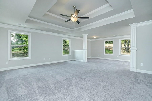 empty room featuring a tray ceiling, ornate columns, healthy amount of natural light, and ornamental molding