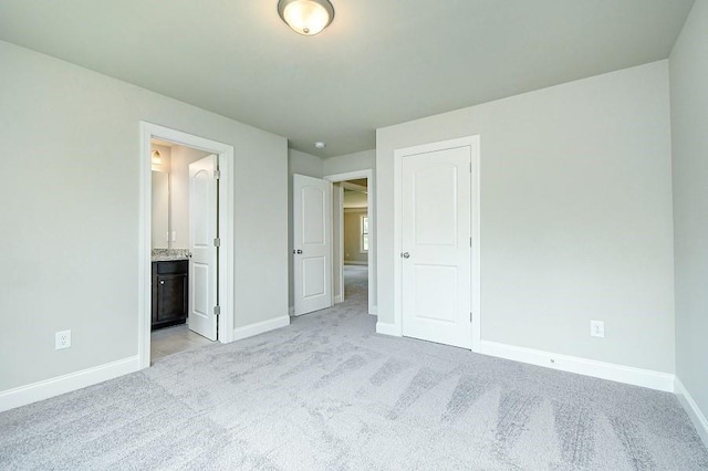unfurnished bedroom with baseboards, light carpet, and connected bathroom