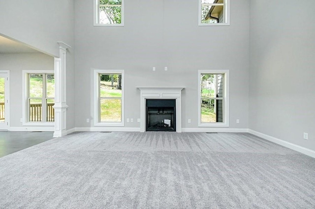 unfurnished living room with carpet floors, a high ceiling, baseboards, decorative columns, and a fireplace