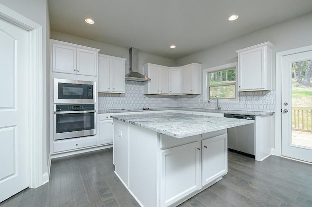 kitchen with appliances with stainless steel finishes, wall chimney exhaust hood, white cabinetry, decorative backsplash, and a center island