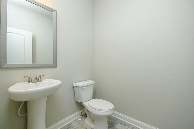 half bathroom featuring marble finish floors, baseboards, toilet, and a sink