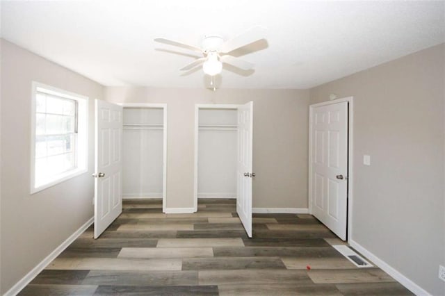 unfurnished bedroom featuring two closets, dark hardwood / wood-style floors, and ceiling fan