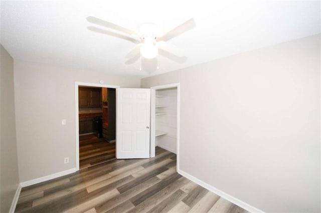 unfurnished bedroom featuring ceiling fan, dark hardwood / wood-style flooring, a walk in closet, and a closet