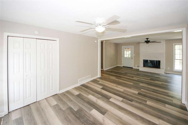 unfurnished living room featuring hardwood / wood-style floors, a brick fireplace, and ceiling fan