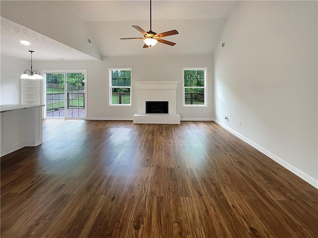 unfurnished living room featuring dark wood-style flooring, a fireplace, baseboards, ceiling fan with notable chandelier, and lofted ceiling
