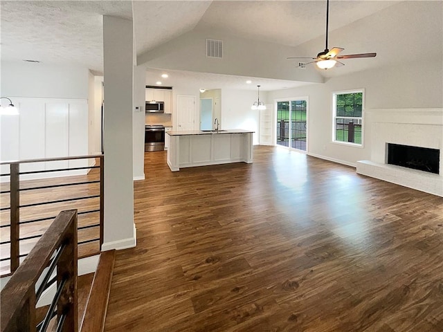 unfurnished living room featuring visible vents, a fireplace, dark wood-style floors, a sink, and ceiling fan with notable chandelier
