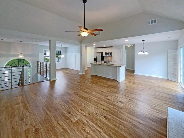 unfurnished living room featuring visible vents, baseboards, high vaulted ceiling, ceiling fan with notable chandelier, and light wood finished floors