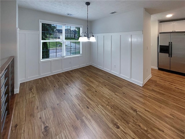 unfurnished dining area with an inviting chandelier, a decorative wall, wood finished floors, and visible vents
