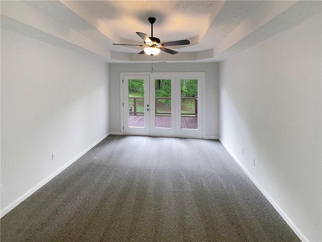 spare room with carpet floors, a tray ceiling, baseboards, and ceiling fan