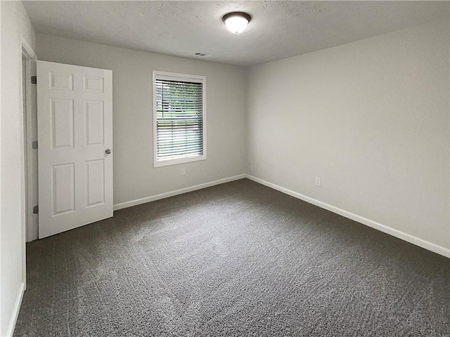 spare room featuring dark carpet, a textured ceiling, baseboards, and visible vents