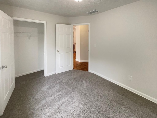 unfurnished bedroom with baseboards, dark colored carpet, and visible vents