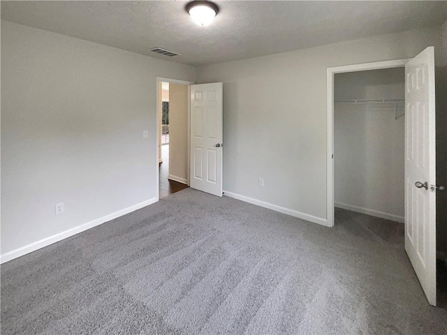 unfurnished bedroom featuring visible vents, a closet, baseboards, dark carpet, and a textured ceiling