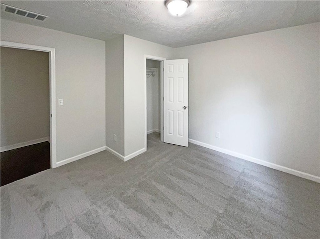 unfurnished bedroom featuring a textured ceiling, visible vents, baseboards, carpet floors, and a closet