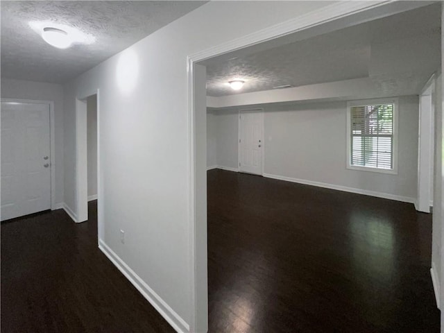 hallway featuring dark wood-style flooring, a textured ceiling, and baseboards