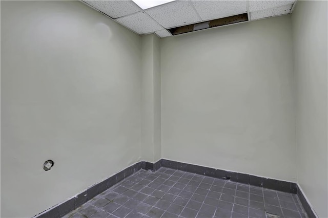 empty room with dark tile patterned flooring, a paneled ceiling, and baseboards
