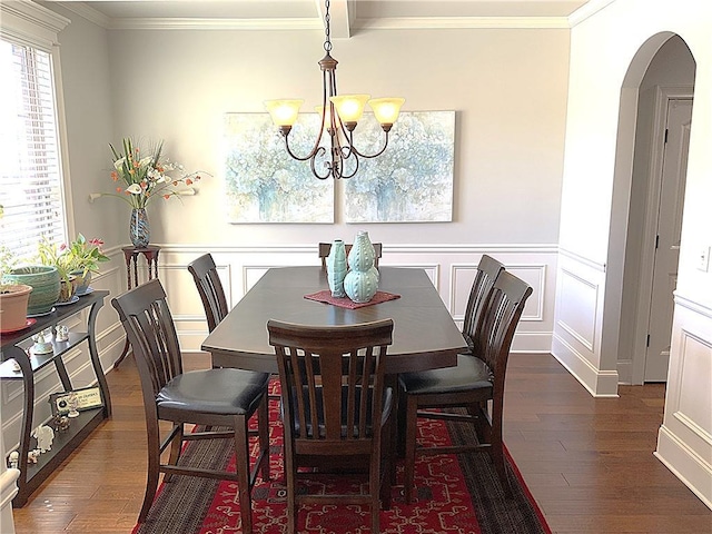 dining area with dark wood-style floors, arched walkways, a wainscoted wall, and crown molding