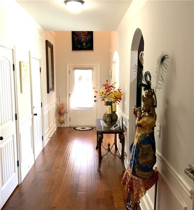 interior space with arched walkways, dark wood-style flooring, wainscoting, and a decorative wall