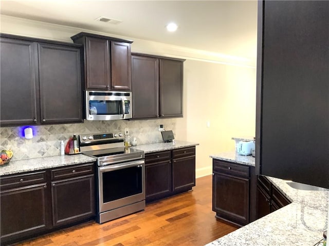 kitchen featuring visible vents, appliances with stainless steel finishes, light stone counters, wood finished floors, and backsplash