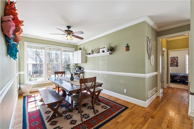 dining area featuring visible vents, baseboards, light wood-style flooring, ceiling fan, and ornamental molding