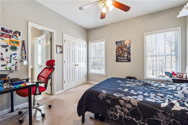 bedroom with baseboards, ceiling fan, a closet, and light colored carpet