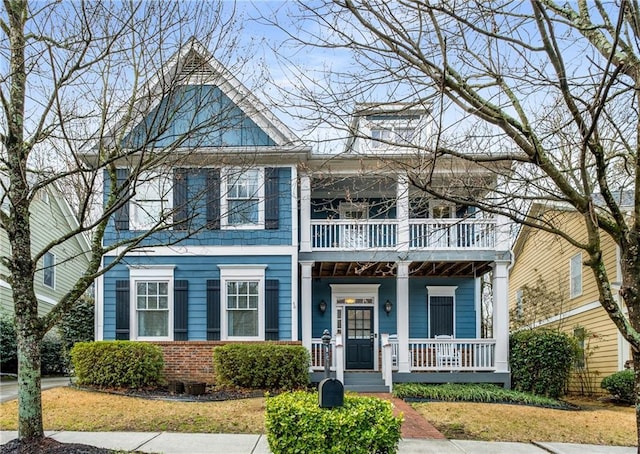 view of front of home featuring a front lawn, a balcony, a porch, and brick siding