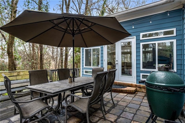 wooden terrace with outdoor dining space, a patio, and area for grilling