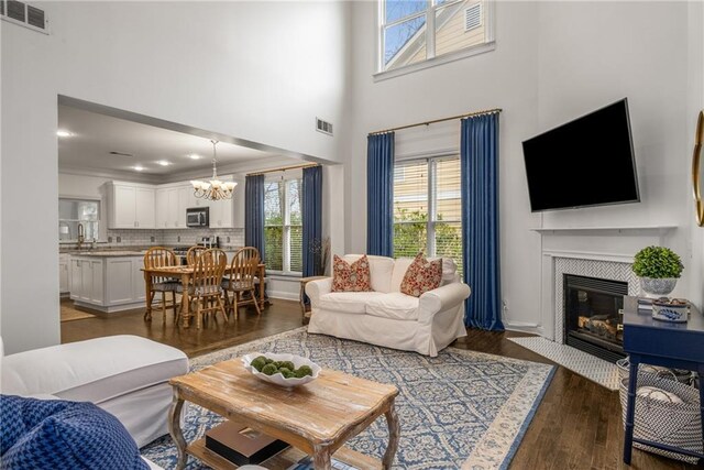 living area with a notable chandelier, visible vents, a fireplace with flush hearth, and wood finished floors