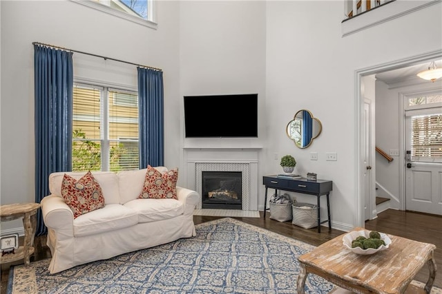 living room with a high ceiling, a fireplace with flush hearth, wood finished floors, and baseboards