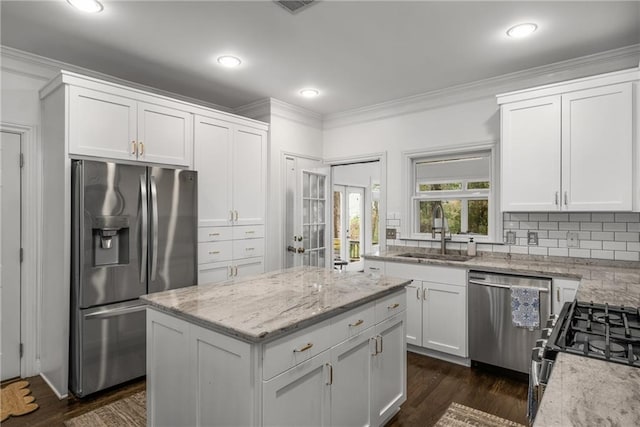 kitchen with light stone counters, ornamental molding, decorative backsplash, a sink, and appliances with stainless steel finishes