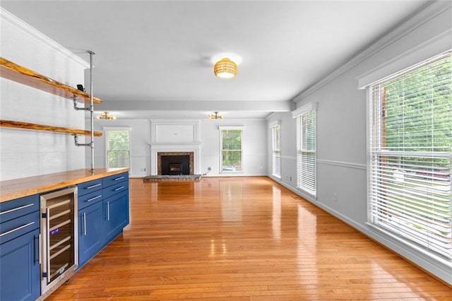 unfurnished living room with wine cooler, a fireplace, light wood finished floors, and a wealth of natural light