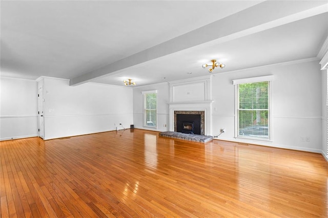 unfurnished living room featuring ornamental molding, a fireplace with raised hearth, hardwood / wood-style flooring, and a wealth of natural light