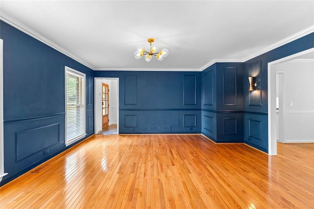 empty room featuring visible vents, ornamental molding, a decorative wall, light wood-style floors, and a chandelier