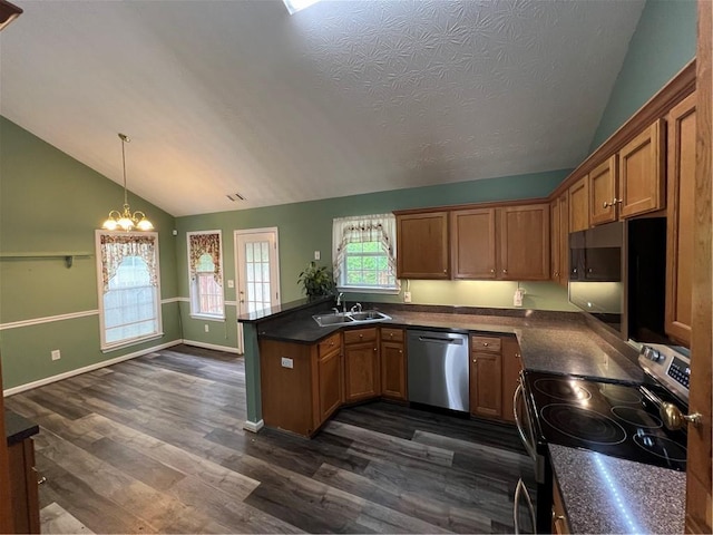 kitchen with dark wood finished floors, lofted ceiling, an inviting chandelier, dark countertops, and appliances with stainless steel finishes