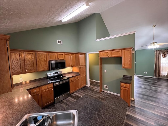 kitchen featuring high vaulted ceiling, dark countertops, brown cabinetry, appliances with stainless steel finishes, and visible vents