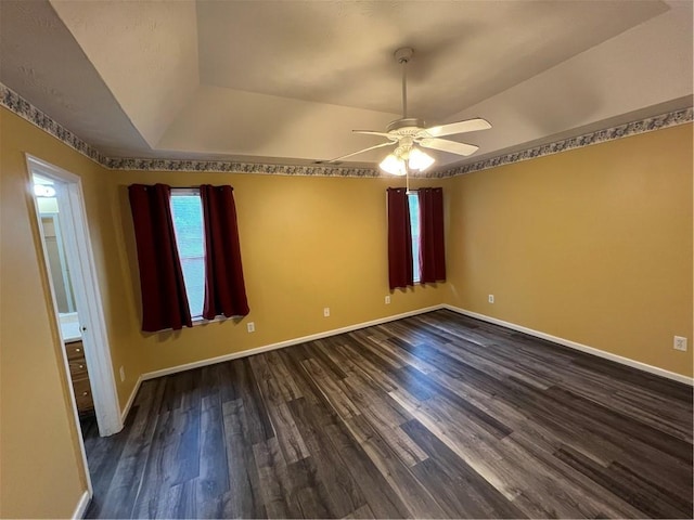 unfurnished room with a tray ceiling, dark wood-style flooring, baseboards, and ceiling fan