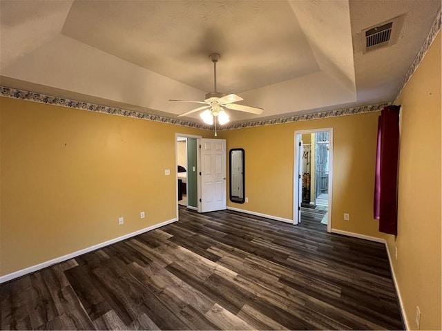 empty room with dark wood finished floors, a raised ceiling, visible vents, baseboards, and ceiling fan