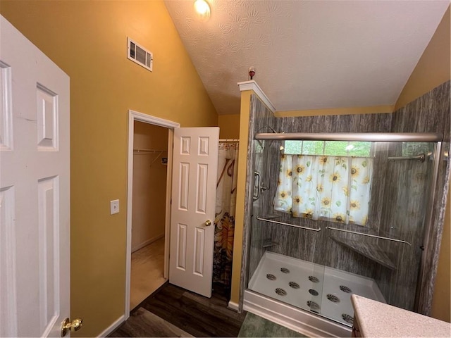 bathroom featuring lofted ceiling, wood finished floors, a shower stall, and visible vents