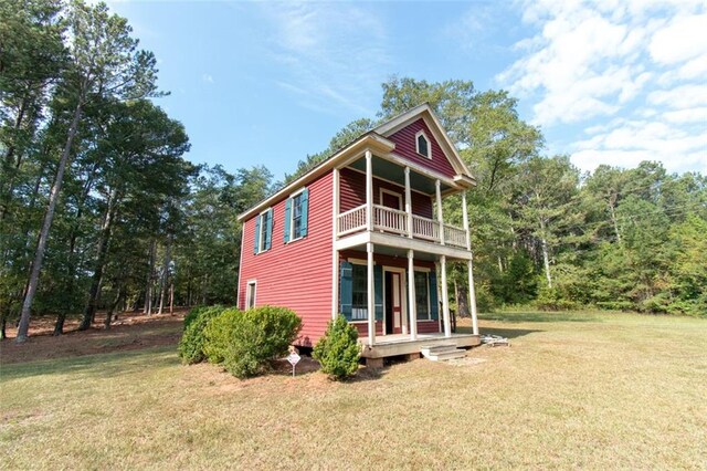 rear view of house featuring a balcony and a yard