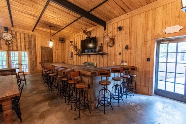 bar featuring concrete flooring, beamed ceiling, wooden walls, and wood ceiling