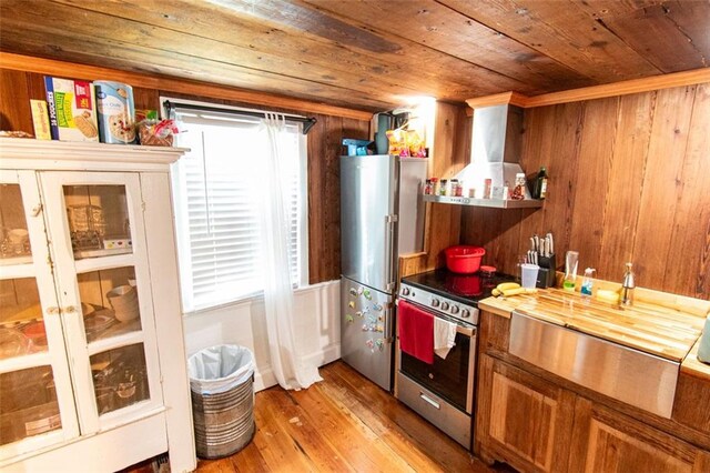 kitchen featuring appliances with stainless steel finishes, a healthy amount of sunlight, wooden walls, and light wood-type flooring