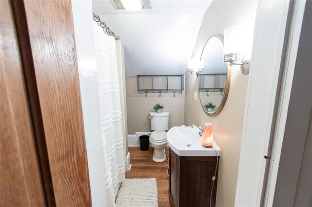 bathroom featuring wood-type flooring, vanity, lofted ceiling, and toilet