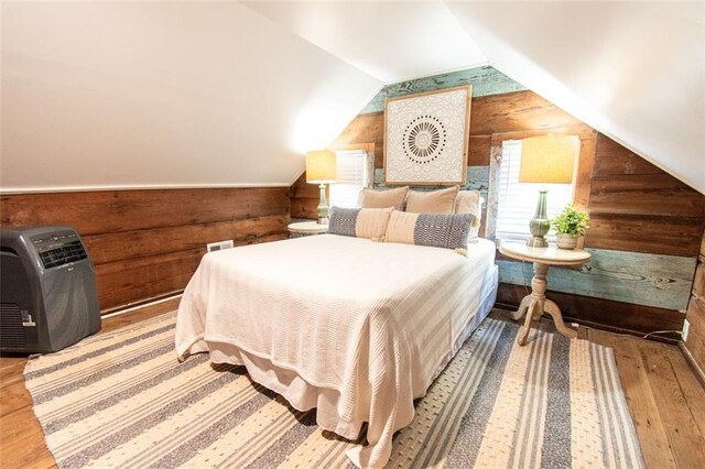 bedroom featuring heating unit, light wood-type flooring, wood walls, and lofted ceiling