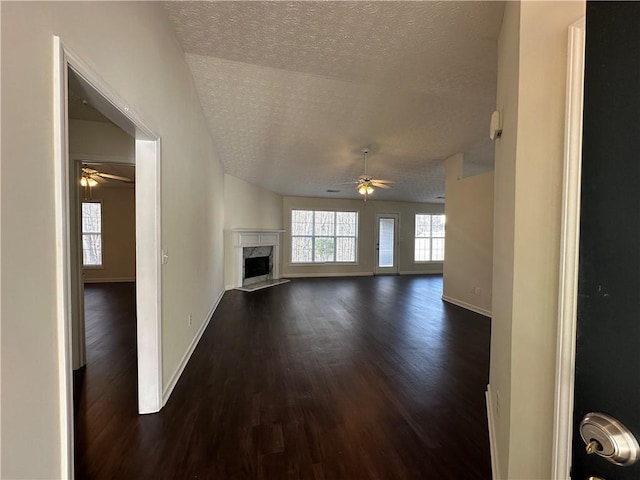 unfurnished living room featuring a ceiling fan, baseboards, a premium fireplace, dark wood-style flooring, and a textured ceiling